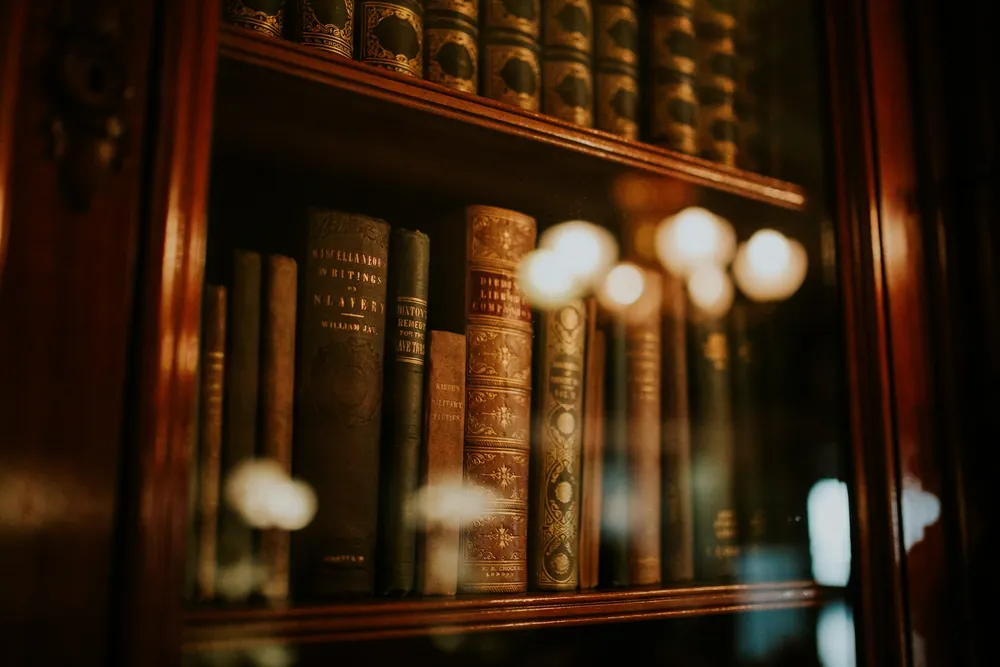 Leather-bound books behind the glass of a lit bookcase.