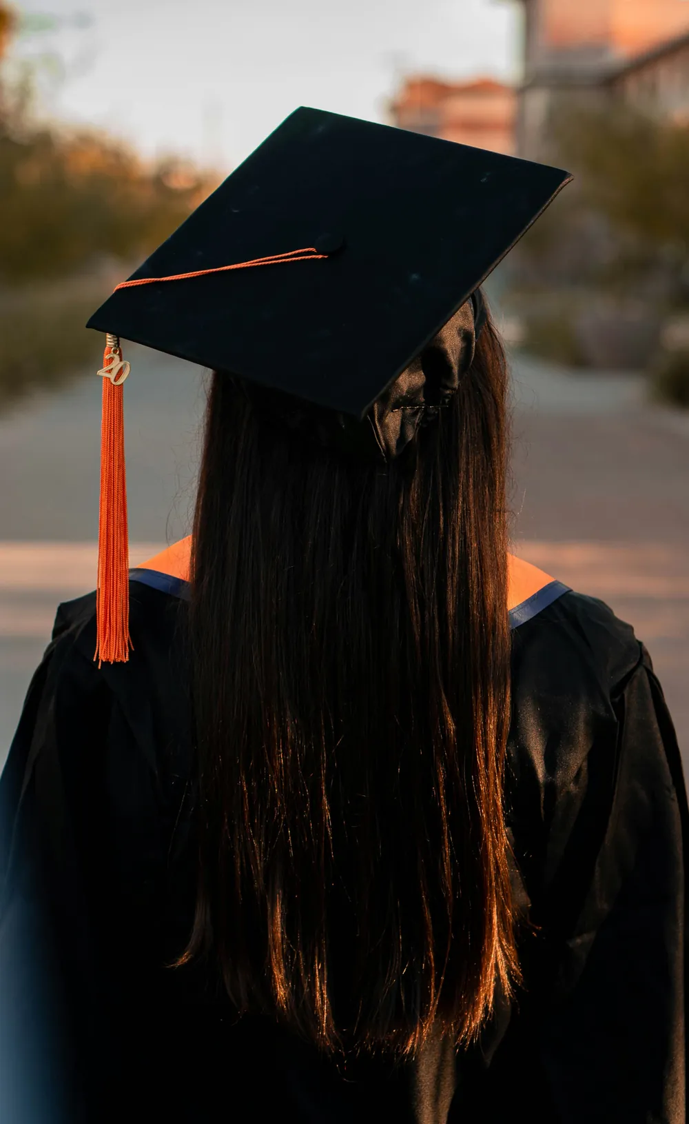 A graduate in cap and gown, seen from behind at golden hour.